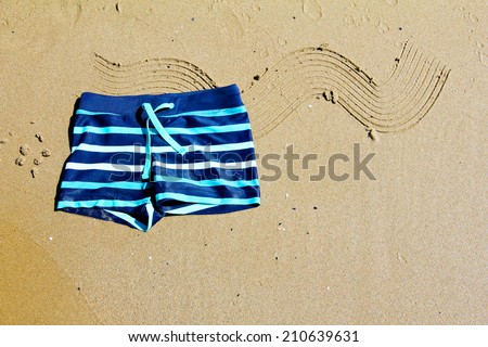 Children's swimming shorts lying on the golden decorated sand on the coast of Mediterranean Sea. Spain.