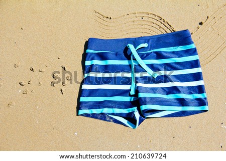 Children\'s swimming shorts lying on the golden sand on the coast of Mediterranean Sea. Spain.