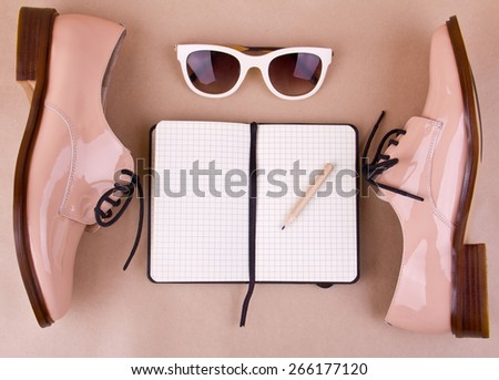 beige patent leather shoes, white sunglasses, small paper notebook with a pencil, beige background. Place for your text.