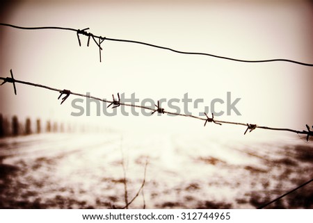 Barbed wire on a winter snowed field background. Sepia filtered.