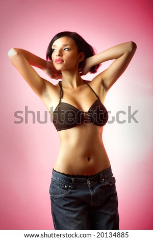 Portrait of beautiful sexy woman with a bikini and a jeans on pink background