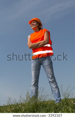 Girl in clothes of the builder worth on a green grass on a background of the blue sky