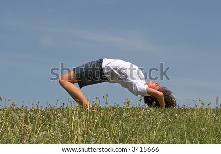 Young pretty girl makes gymnastics on a green grass on a background of the blue sky