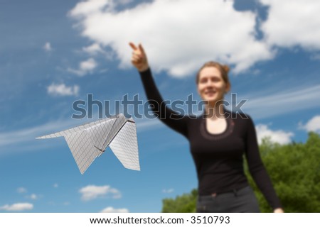 Flying paper plane in the foreground and the nice girl on a background of the beautiful blue sky with clouds