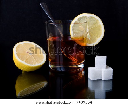Glass with tea, the spoon, sugar and a lemon on a black reflecting surface