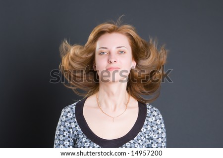 Portrait of the beautiful smiling girl with fluttering hair on a dark background