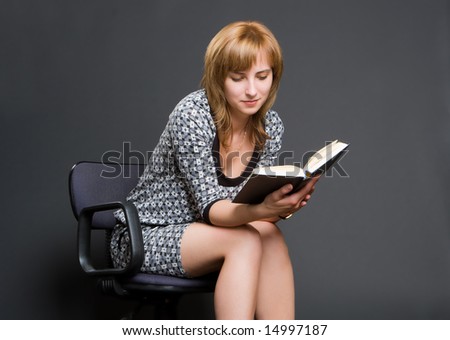 Woman reads the book sitting on office armchair on a dark background