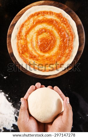 balls of fresh pizza dough in hand and tomato sauce on pizza base.