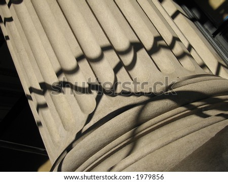 A stone base of a Ionic column crisscrossed by lines of shadow.