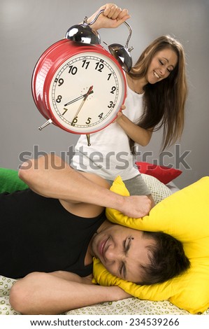 Beautiful Young couple sleeping in bed in the morning. Sleepy boyfriend waking up with alarm clock.