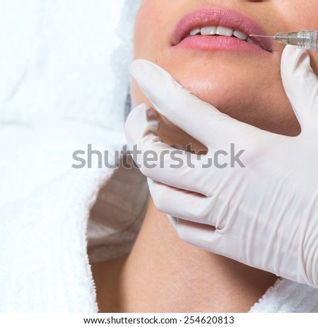Cosmetic injection to the pretty caucasian woman face and beautician hands with syringe