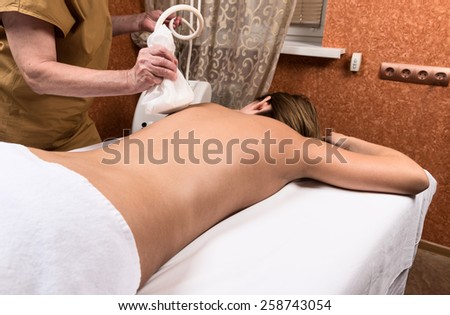 Young naked woman undergoing modern massage procedure at spa centre