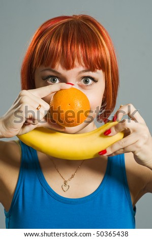 Red-haired girl with banana and orange in her hands. Focus is on the fruits forming a smiley :)