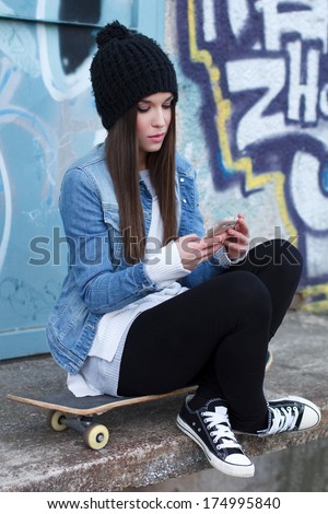 Trendy teenager with smartphone and skateboard, outdoor
