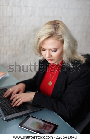 Blonde businesswoman working on laptop, looking on tablet online growth chart