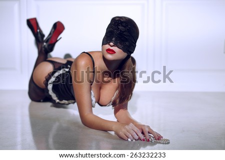Sexy woman in underwear and lace eye cover kneeling on floor with pearls