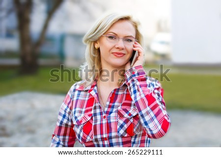 Blonde woman in flannel shirt and glasses calling outdoor, young businesswoman