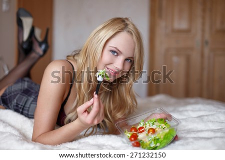 Sexy blonde student in college eating salad on bed