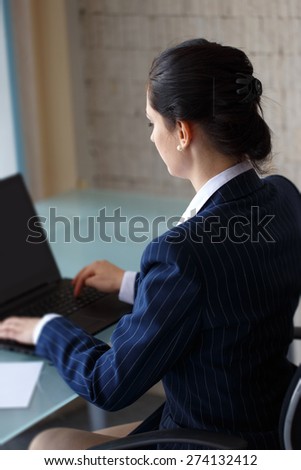 Confident businesswoman typing on laptop in office, back view