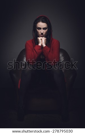 Sexy woman in red sweater at night sitting in sofa, little red riding hood style