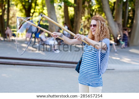 Woman with curly hair pull soap bubbles in park