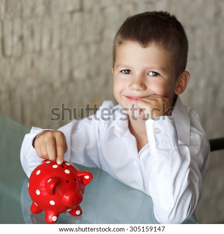 Little boy insert coin into red dotted piggy bank in office