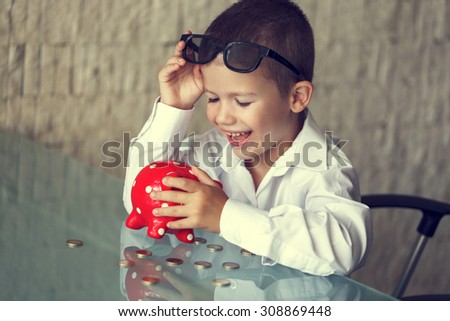Happy little manager boy with coins and piggy bank laughing in office, retro style