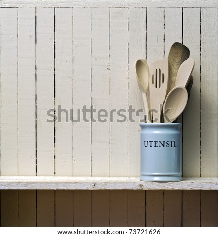 Kitchen cooking utensils; wooden spatulas etc in china storage pot; on wooden shelf against rustic kitchen wall; excellent copy space over wall area