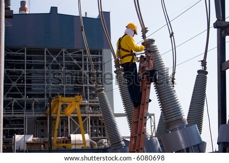 Worker at the switch yard for maintenance work with power plant at the background