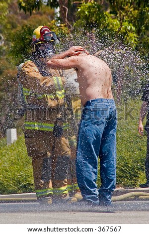 A firefighter spraying a man down in order to wash him clean of any potential chemical contamination.