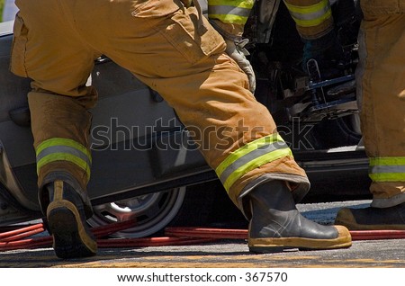 A team of firefighters prying a door off the car with the jaws of life.