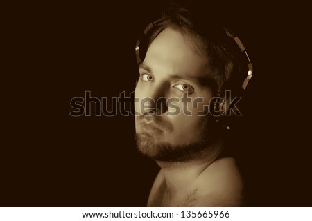 vintage-like low key portrait of young man with beard and hairy shoulders in headphones