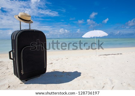 black suitcase sun hat and white sunshade at the beach