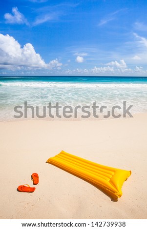 yellow air mattress and orange flip-flops at a beautiful beach with a turquoise sea