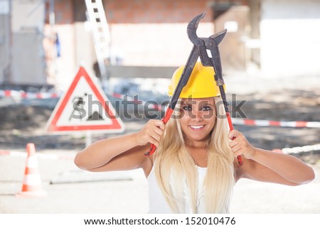 young female builder on the construction site posing with pipe tongs or gaspipe pliers