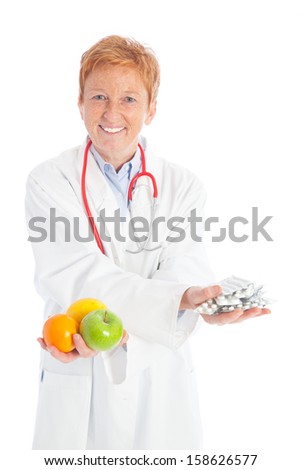elder female practitioner doctor with a red stethoscope and a white doctorÂ´s overall holding an apple, orange, lemon and pills in her hands, offering healthy food or medicine to choose