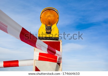 yellow signal lamp warning  against a building site with red and white barrier or warning tape before a blue sky
