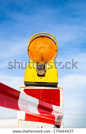 yellow signal lamp warning  against a building site with red and white barrier or warning tape before a blue sky