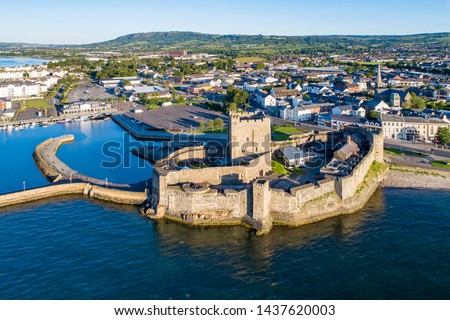 Medieval Norman Castle in Carrickfergus near Belfast in sunrise light. Aerial view with marina, yachts, parking and town 