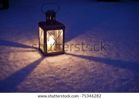 Christmas Lantern A candle lit inside a lantern sitting on the snow in the dark