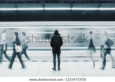 Long exposure picture with lonely young man shot from behind at subway station with blurry moving train and walking people in background 商業照片 © 