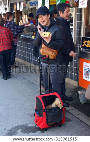 OSAKA, JAPAN - MARCH 25, 2012: Young japanese man talking on the phone. He just bought take away fast food in the street. His dog is sitting beside in pet carrier