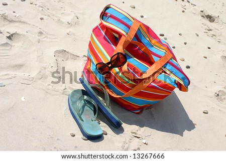 Beach items - flip-flop, beach bag and sunglasses lying on the sand