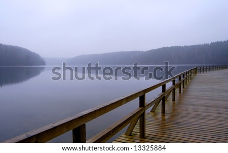 Lonely pier with rail on the foggy lake, tranquil late autumn scenery