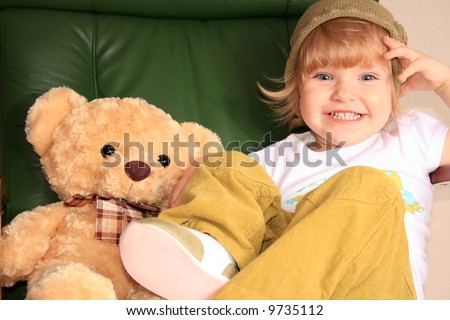 The little girl poses in the big green leather armchair with a toy bear