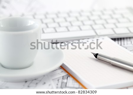 keyboard, white cup, notepad, pen ,and architectural drawings of the modern house
