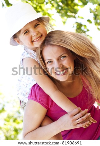 Mother giving her daughter piggyback ride in the park