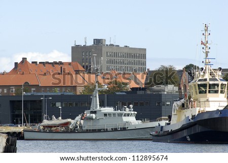 Tug and military ship in Fredericia harbour close to the city with big grey hospital in the background.