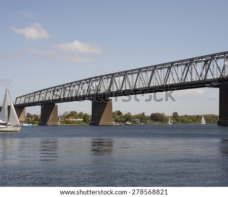 Boats on water and bridge with bridge-walking bridge and small people in gray coveralls on top of the Old Little Belt Bridge.