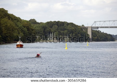 Active man kayaking on Little Belt close to old bridge and small harbor in Denmark